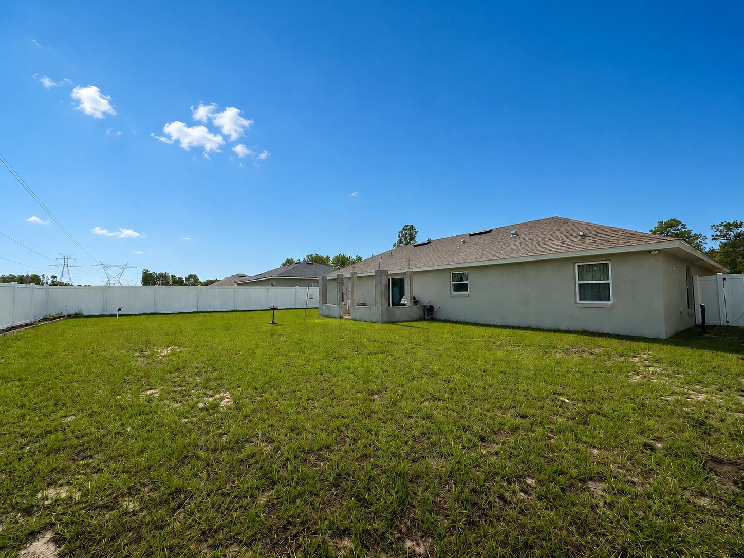 A view of a backyard with a white vinyl fence and a house exterior — 15211 SW 65th Ter Road, Ocala FL 34473, OCALA, FL