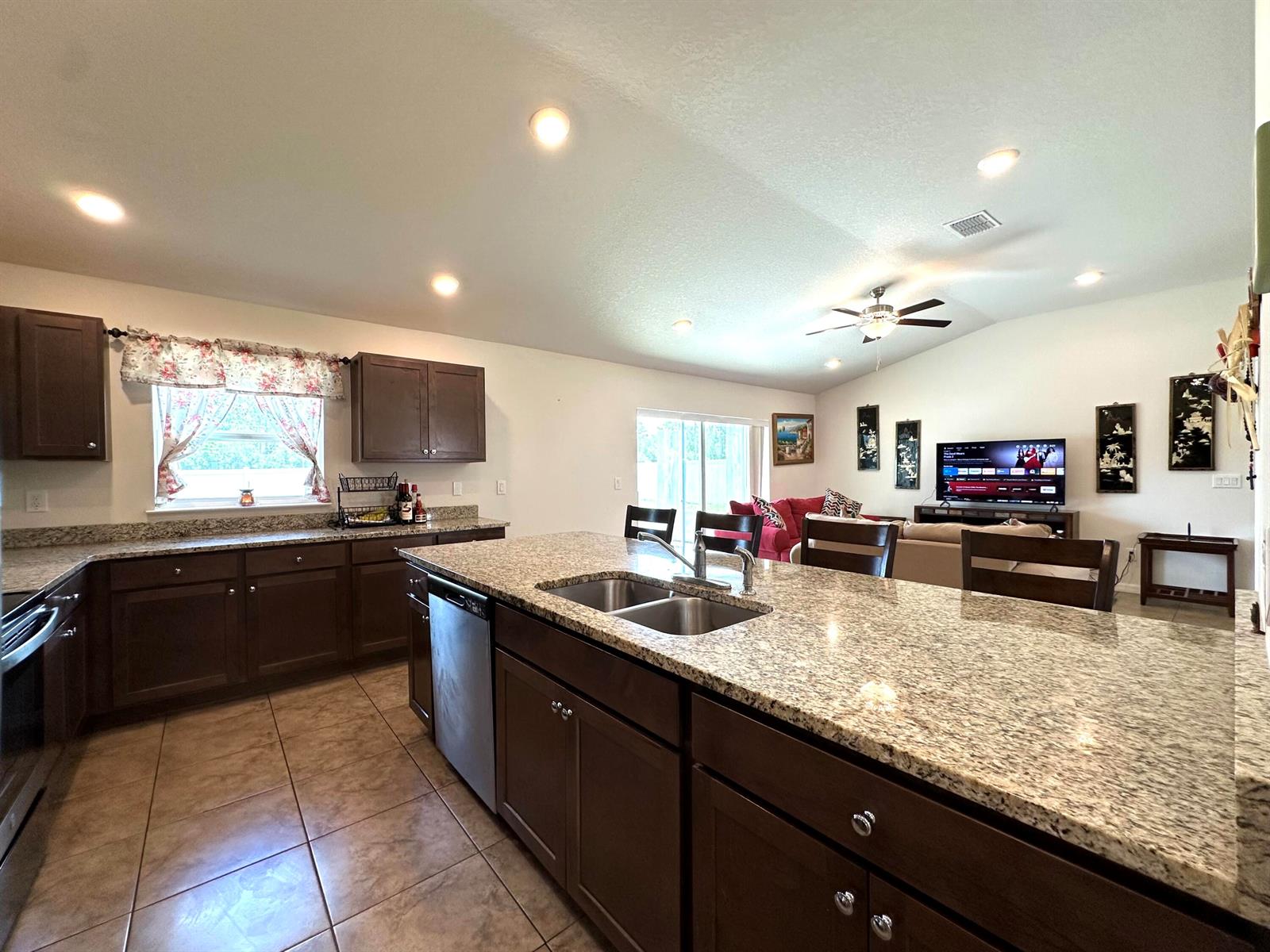 A kitchen with dark wood cabinets, granite countertops, and an island opens to a living room — 15211 SW 65th Ter Road, Ocala FL 34473, OCALA, FL