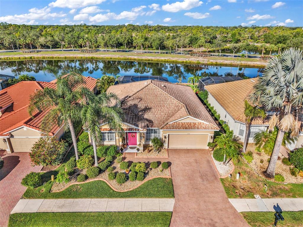 An aerial view of a suburban house with a tile roof, driveway, and waterfront backyard — 11360 DANCING RIVER DRIVE, VENICE, FL
