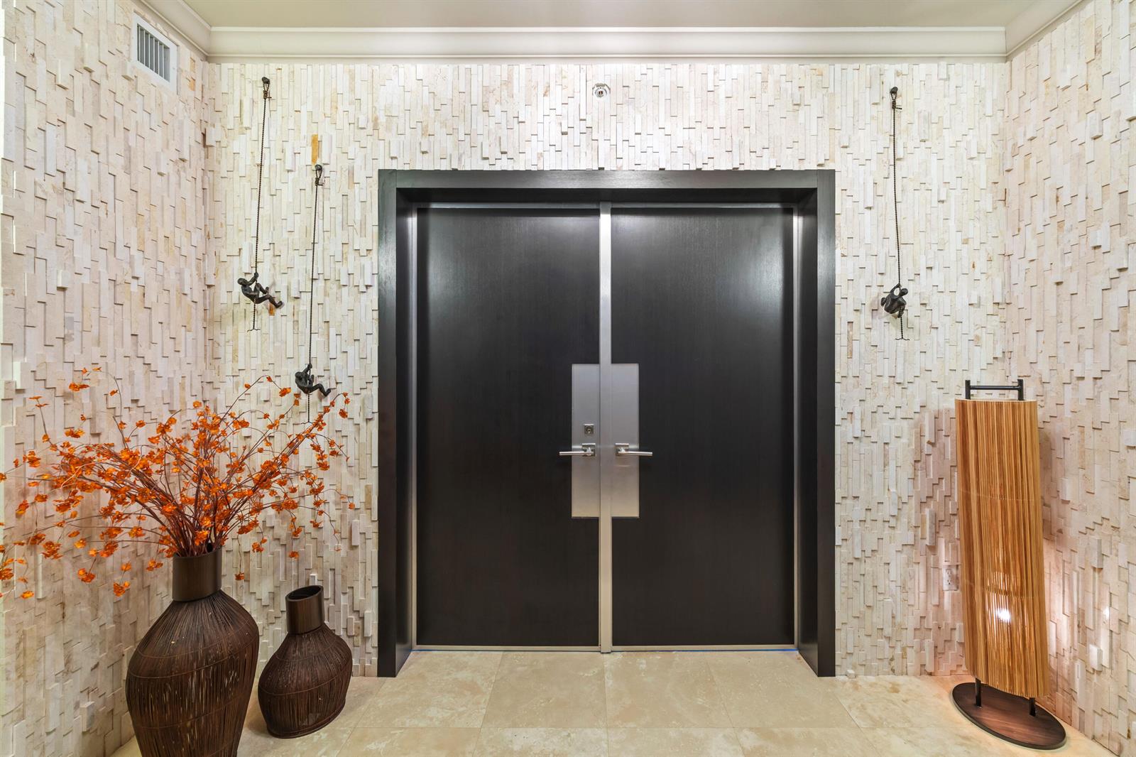 A modern entryway features double dark wood doors, textured stone walls, and decorative climbing figures — 3101 S Ocean Drive # 3105, Hollywood FL 33019, HOLLYWOOD, FL