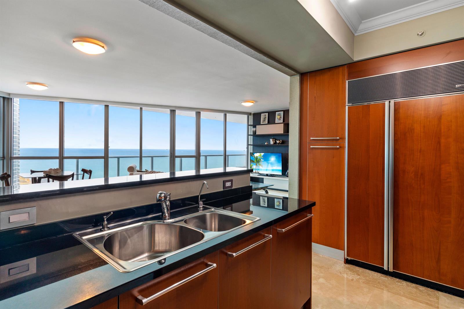 A kitchen with dark countertops and wood cabinets overlooks a living area and ocean view — 3101 S Ocean Drive # 3105, Hollywood FL 33019, HOLLYWOOD, FL