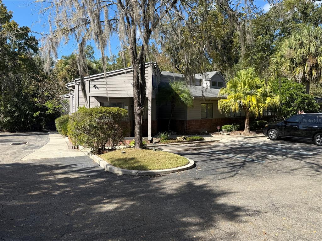 A gray building with a brick base sits behind a parking lot and trees — 1034 NW 57TH STREET, GAINESVILLE, FL
