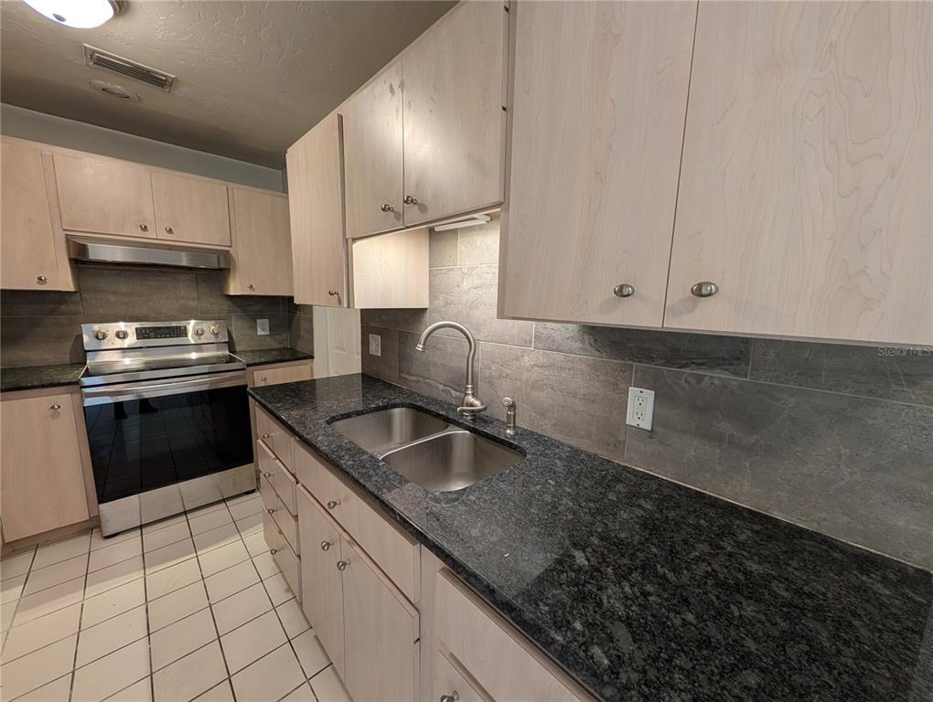 A kitchen features light wood cabinets, dark granite countertops, a stainless steel stove, and tile flooring — 4031 IOLA DRIVE, SARASOTA, FL