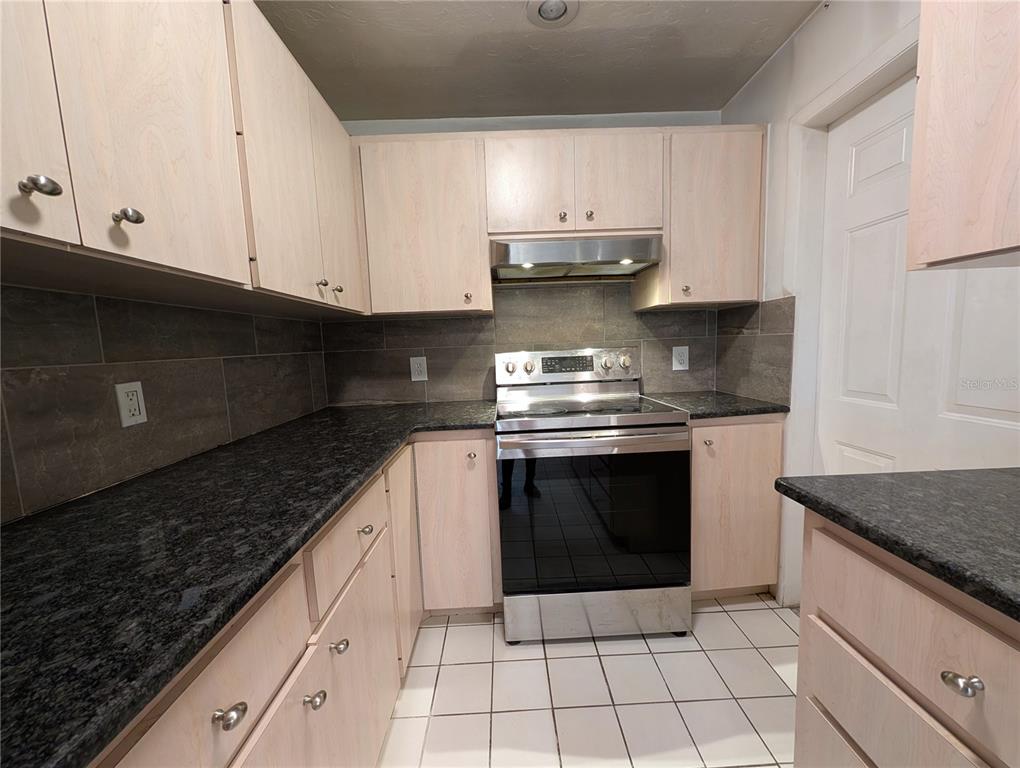 A kitchen features light wood cabinets, dark granite countertops, a stainless steel stove, and tile flooring — 4031 IOLA DRIVE, SARASOTA, FL