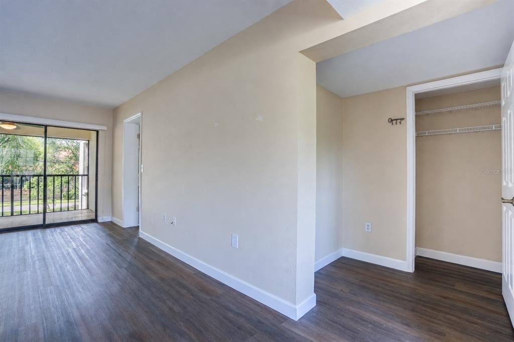 An interior view of a room with wood-look flooring, a closet, and a sliding glass door — 2497 HERON TERRACE UNIT 203C, CLEARWATER, FL