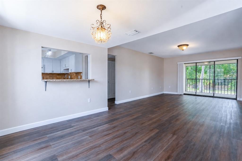 An open-concept living area features dark wood-look flooring, a kitchen pass-through, and sliding glass doors — 2497 HERON TERRACE UNIT 203C, CLEARWATER, FL