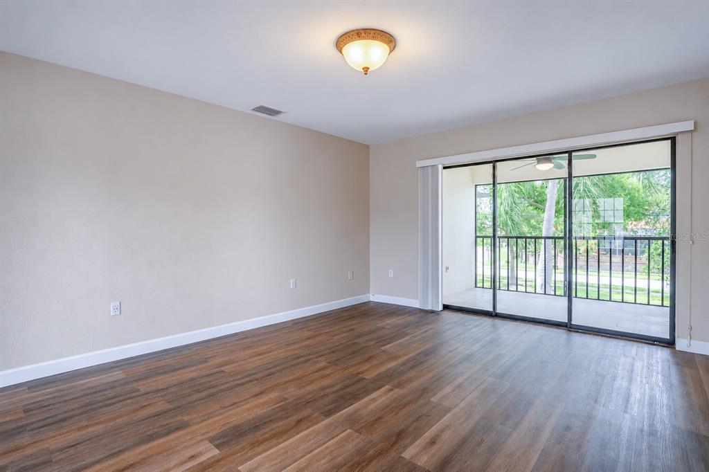 An empty room with wood-look flooring, a ceiling light, and a sliding glass door to a balcony — 2497 HERON TERRACE UNIT 203C, CLEARWATER, FL