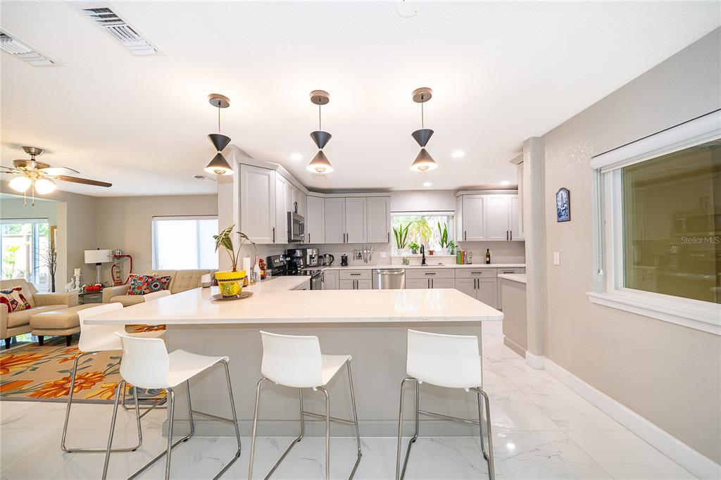 A kitchen with light gray cabinets, white countertops, and three bar stools at an island — 502 OAK LANE, MAITLAND, FL