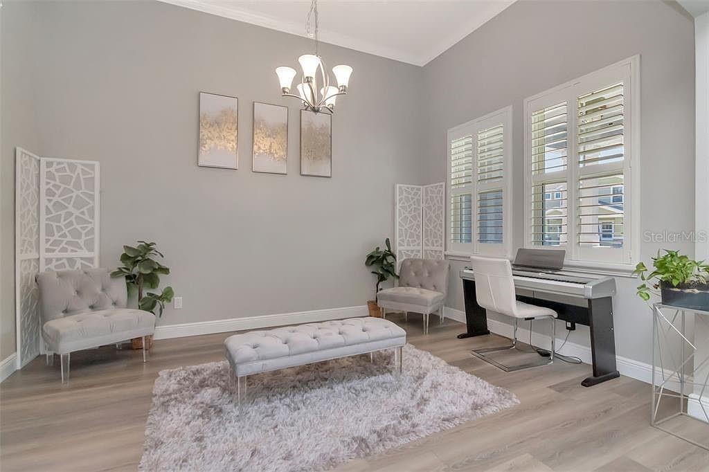 A light-filled room features gray walls, wood-look flooring, a tufted bench, and a digital piano — 19419 AUTUMN CHASE COURT, LAND O LAKES, FL