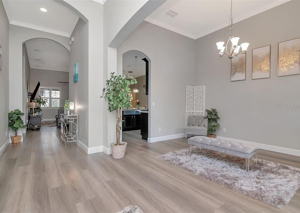 A bright, open-concept living area features light wood flooring, arched entryways, and a chandelier — 19419 AUTUMN CHASE COURT, LAND O LAKES, FL