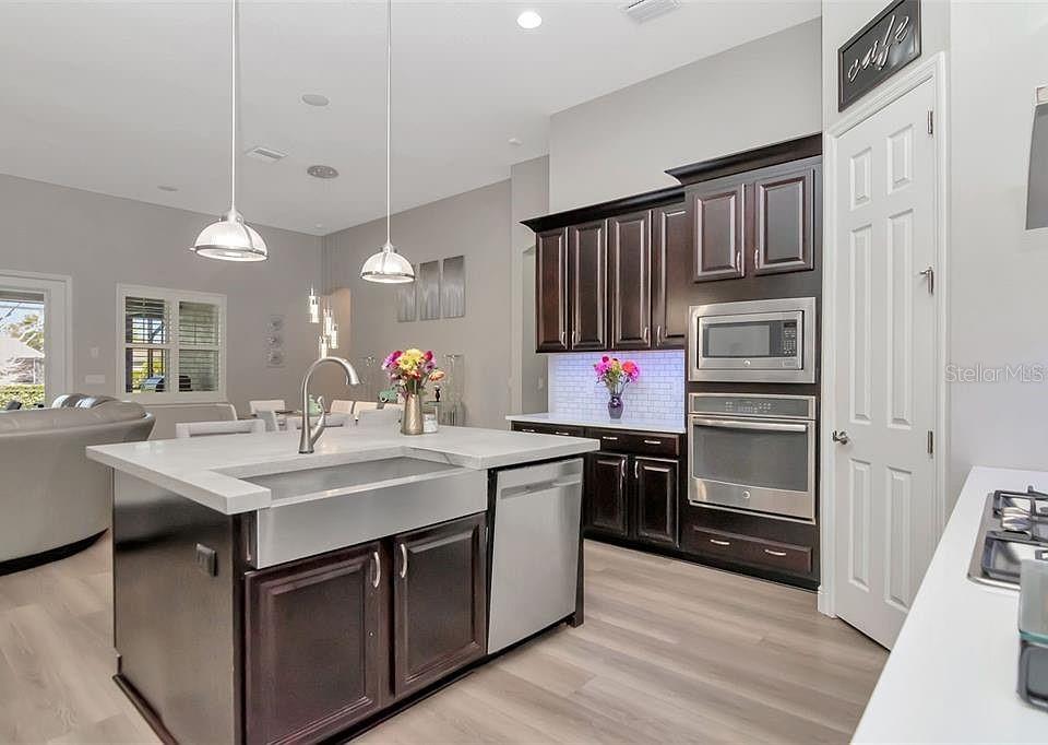 A modern kitchen features dark wood cabinets, a stainless steel farmhouse sink, and an island — 19419 AUTUMN CHASE COURT, LAND O LAKES, FL