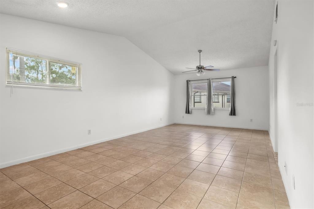 An empty room with vaulted ceilings, beige tile flooring, and two windows with curtains — 831 ORCHID SPRINGS DRIVE UNIT #831, WINTER HAVEN, FL