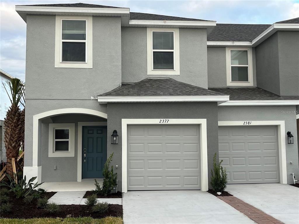 A two-story gray townhouse exterior features a blue front door and two attached garages — 2377 PARAVANE WAY, WESLEY CHAPEL, FL