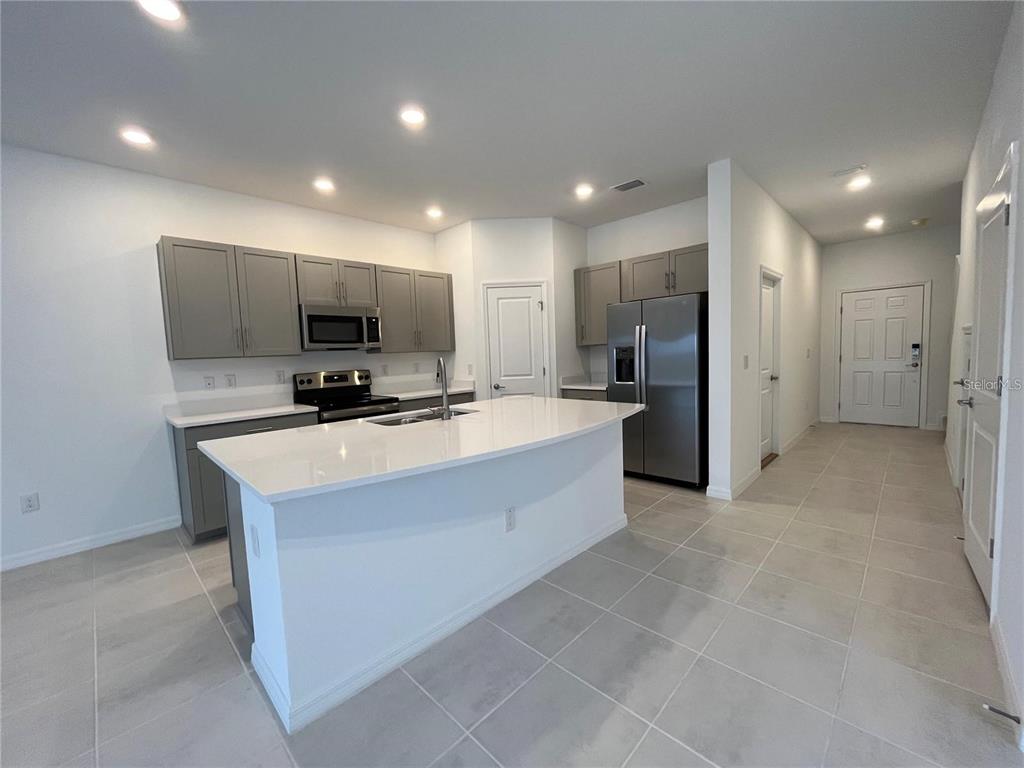 A modern kitchen features gray cabinets, white countertops, a central island, and stainless steel appliances — 2377 PARAVANE WAY, WESLEY CHAPEL, FL