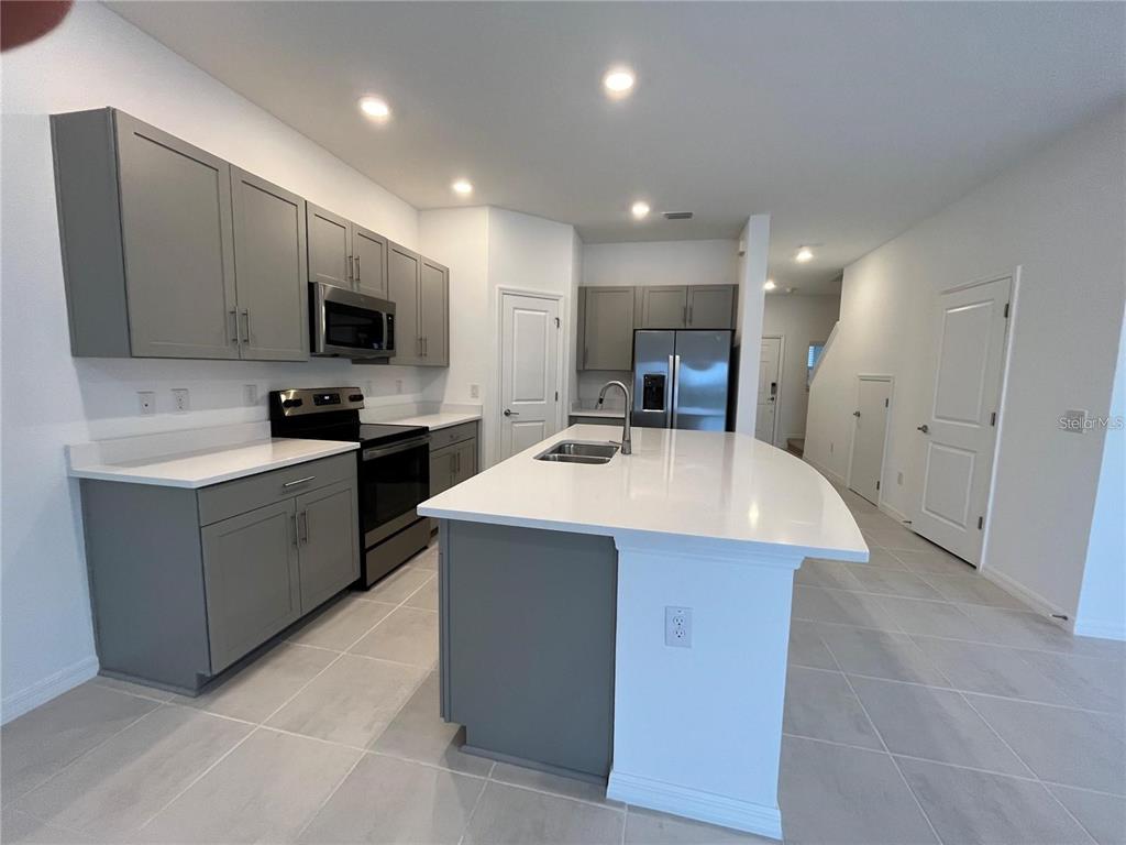 A modern kitchen features gray cabinets, white countertops, stainless steel appliances, and a central island — 2377 PARAVANE WAY, WESLEY CHAPEL, FL