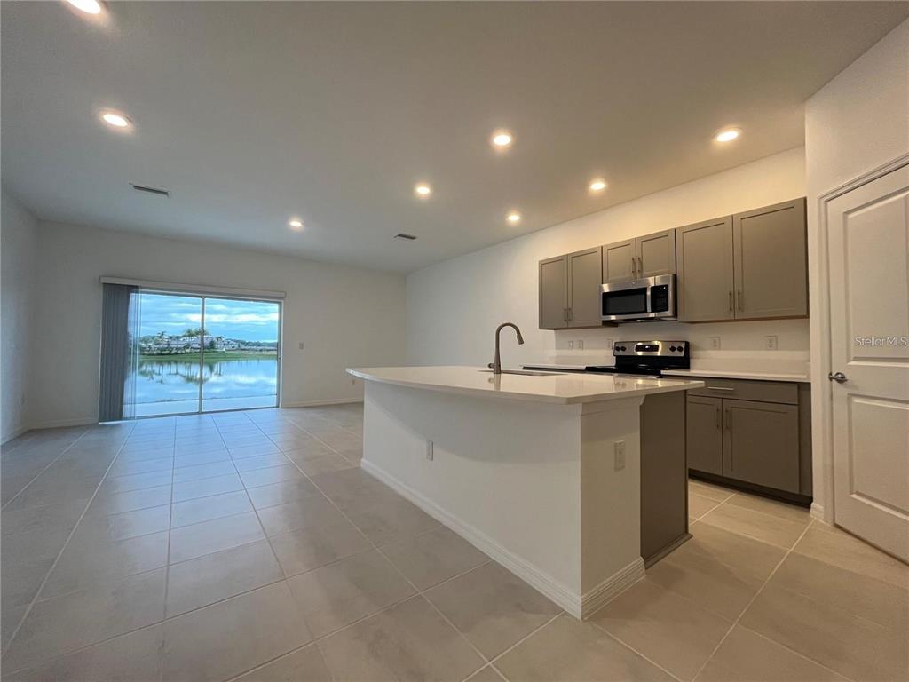 A kitchen with gray cabinets and a white island overlooks a lake through sliding doors — 2377 PARAVANE WAY, WESLEY CHAPEL, FL