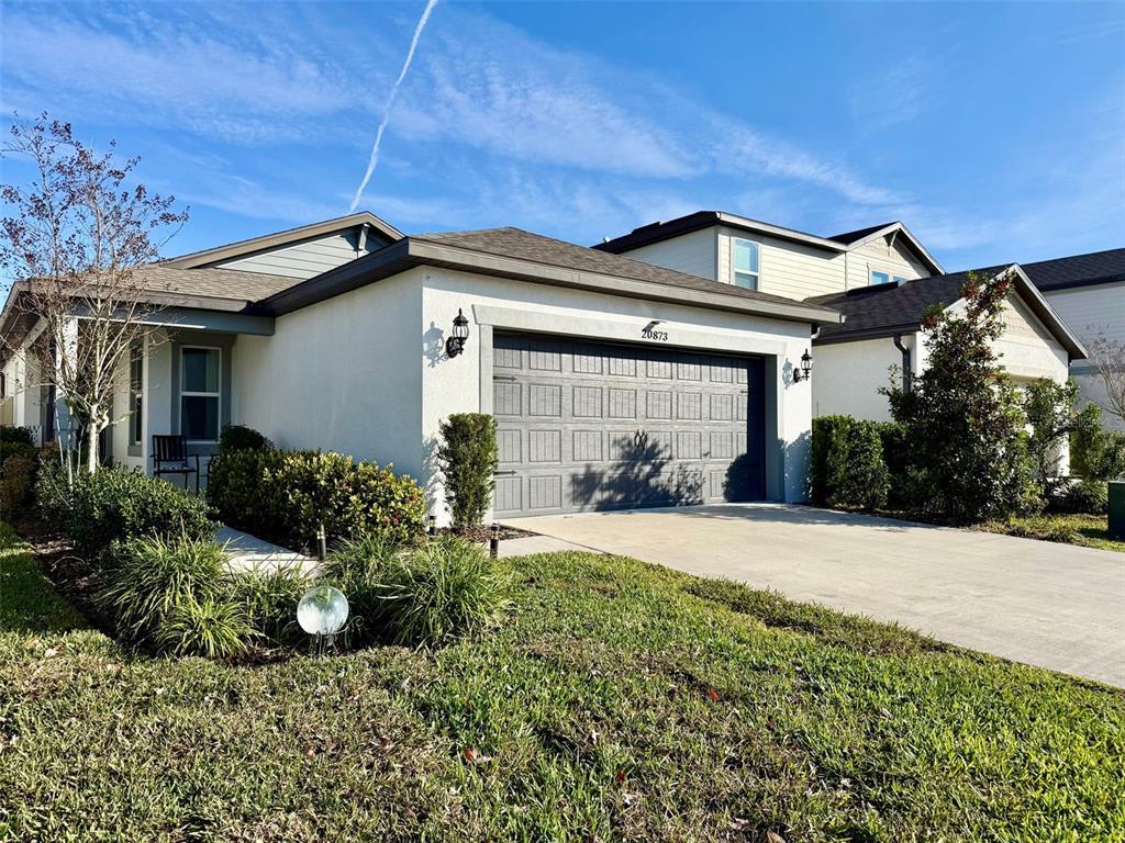 A single-story house with a gray garage door, white stucco walls, and a landscaped yard — 20873 DRAKE ELM DRIVE, LAND O LAKES, FL