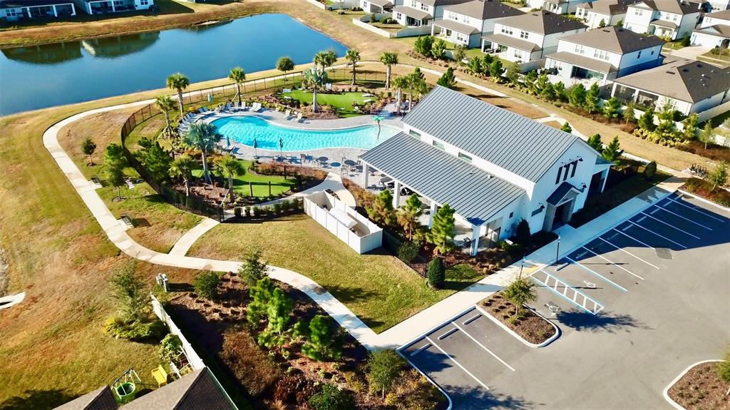 An aerial view shows a community clubhouse with a swimming pool, parking lot, and pond — 20873 DRAKE ELM DRIVE, LAND O LAKES, FL