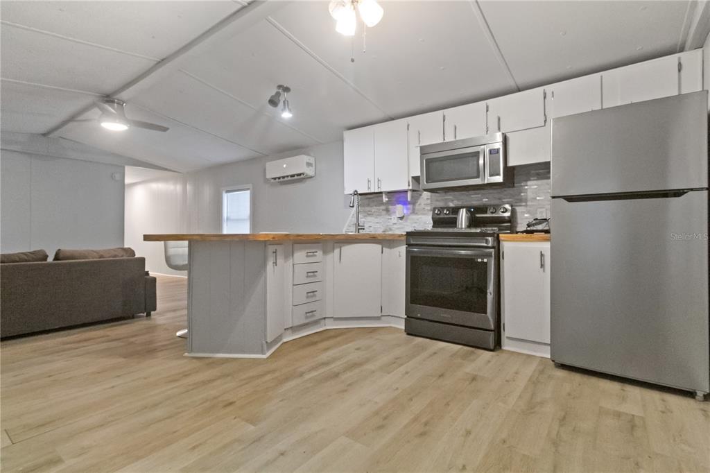 This kitchen features white cabinets, stainless steel appliances, a wood-topped island, and light wood flooring — 11301 EDISON AVENUE, NEW PORT RICHEY, FL