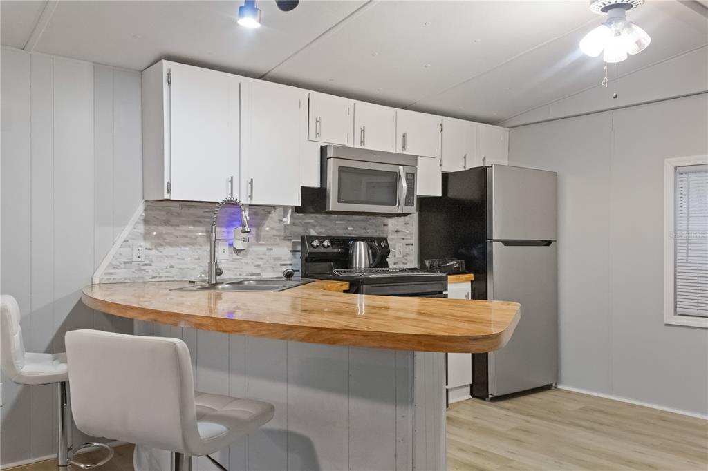 A kitchen features white cabinets, a wooden countertop, stainless steel appliances, and two bar stools — 11301 EDISON AVENUE, NEW PORT RICHEY, FL