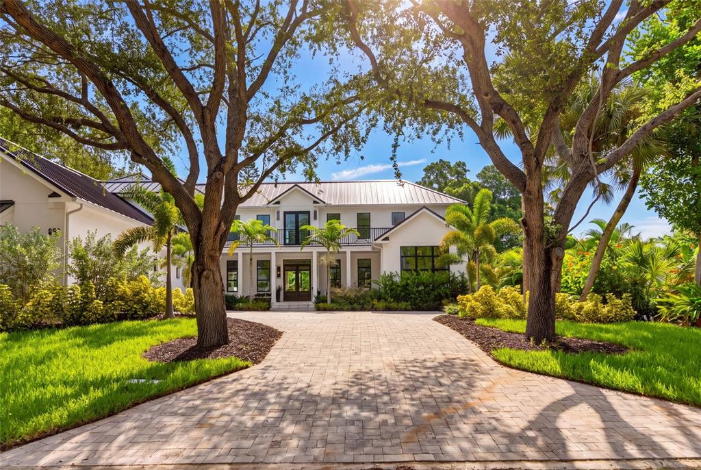 A two-story white house with a metal roof and a paved driveway framed by trees — 656 TROPICAL CIRCLE, SARASOTA, FL