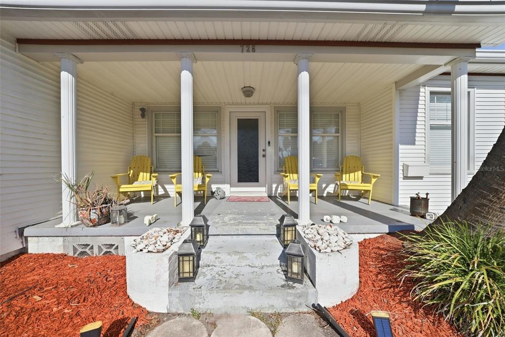 A covered front porch features four yellow chairs, white columns, and concrete steps with lanterns — 726 MANDALAY AVENUE, CLEARWATER BEACH, FL