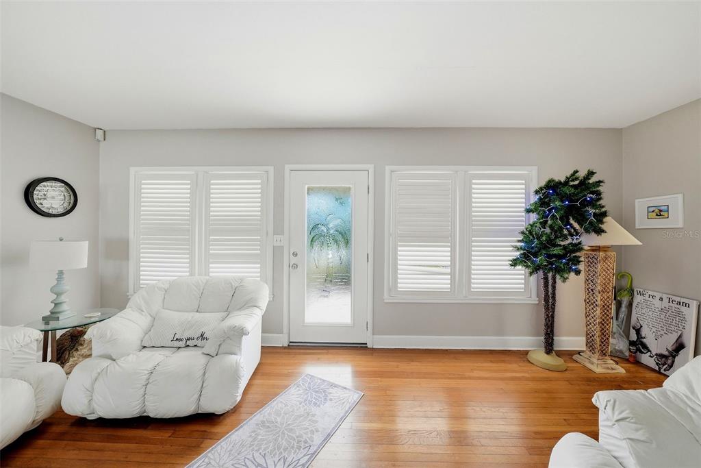 A living room features white furniture, hardwood floors, plantation shutters, and a front entry door — 726 MANDALAY AVENUE, CLEARWATER BEACH, FL