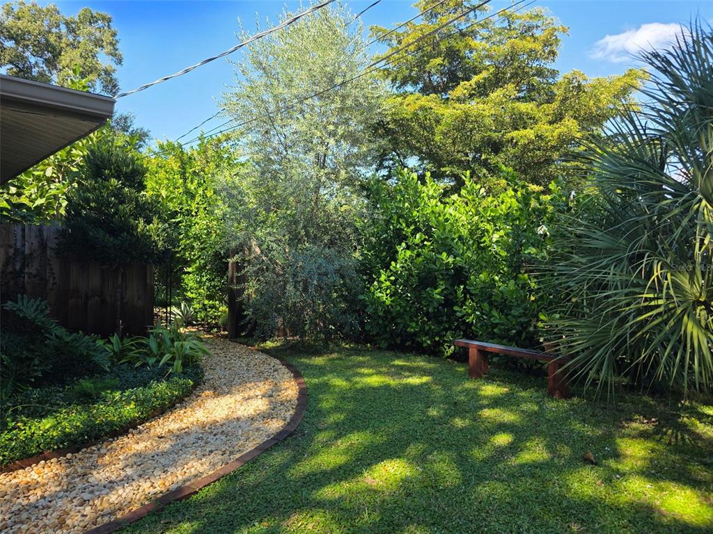 A gravel path curves through a grassy backyard with a wooden bench and dense landscaping — 4718 CRYSTAL AVENUE, SARASOTA, FL