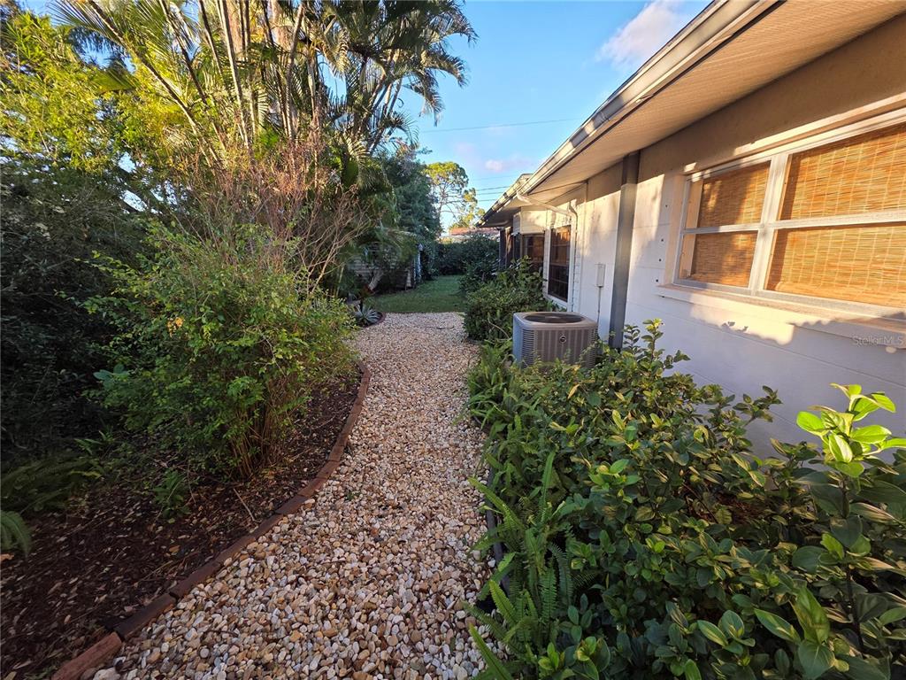 A gravel path runs alongside a house exterior featuring an air conditioning unit and landscaping — 4718 CRYSTAL AVENUE, SARASOTA, FL