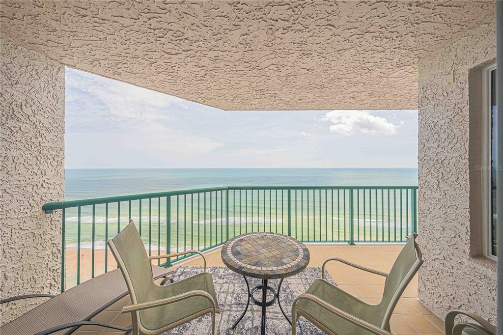 A balcony with a tiled table and two chairs overlooks the ocean and beach — 3315 S ATLANTIC AVENUE UNIT 1707, DAYTONA BEACH SHORES, FL