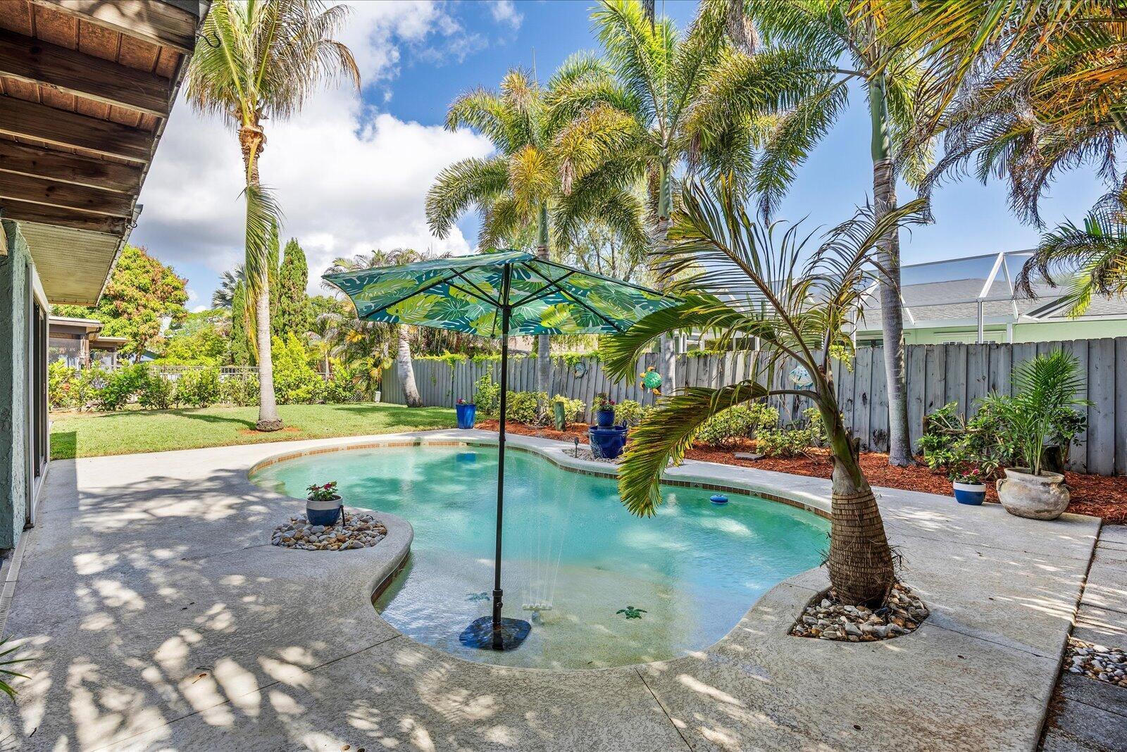 A backyard features a kidney-shaped swimming pool, a patterned umbrella, and several palm trees — 687 NE Maranta Terrado, Jensen Beach FL 34957, JENSEN BEACH, FL