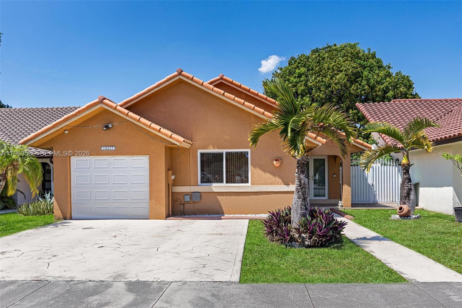 A single-story house with a tan stucco exterior, a white garage door, and palm trees — 14217 SW 102nd St, Miami FL 33186, MIAMI, FL