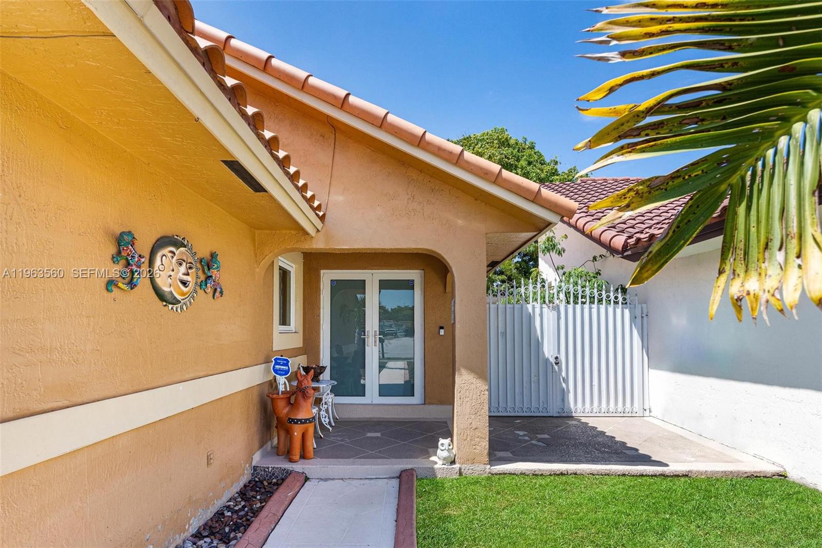 The exterior of a house features a covered entryway, double glass doors, and decorative wall art — 14217 SW 102nd St, Miami FL 33186, MIAMI, FL