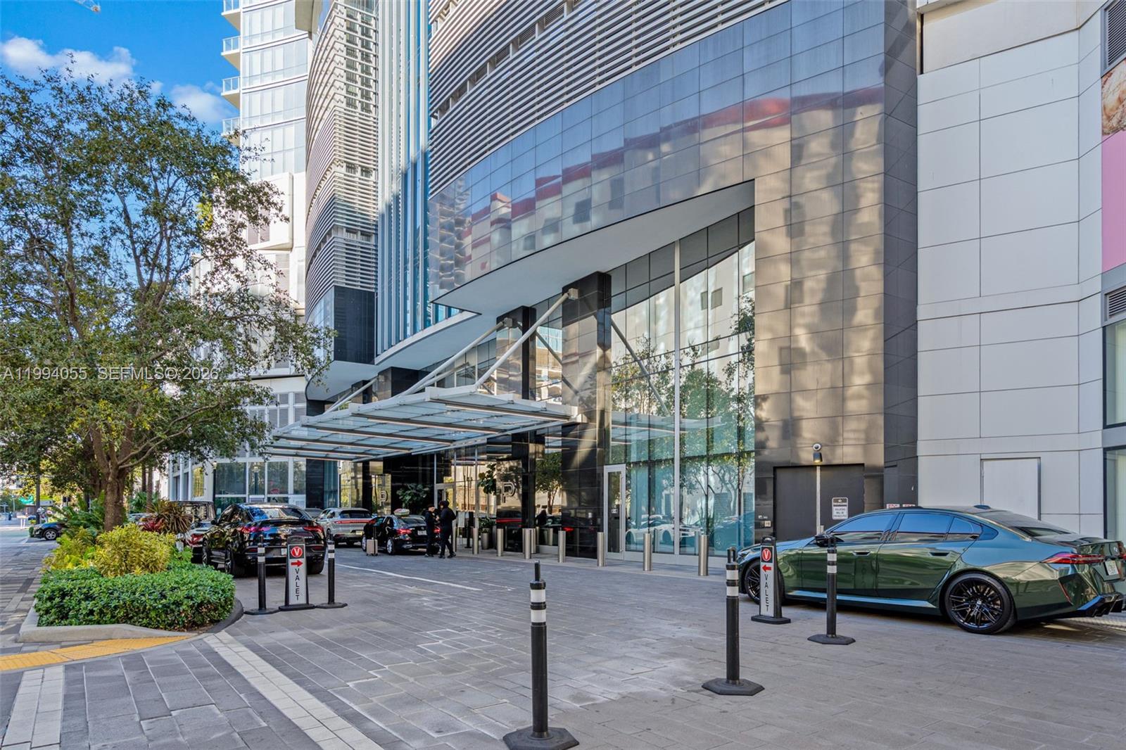 A modern building entrance features a glass canopy, valet parking area, and reflective glass facade — 851 NE 1st Ave # 1205, Miami FL 33132, MIAMI, FL
