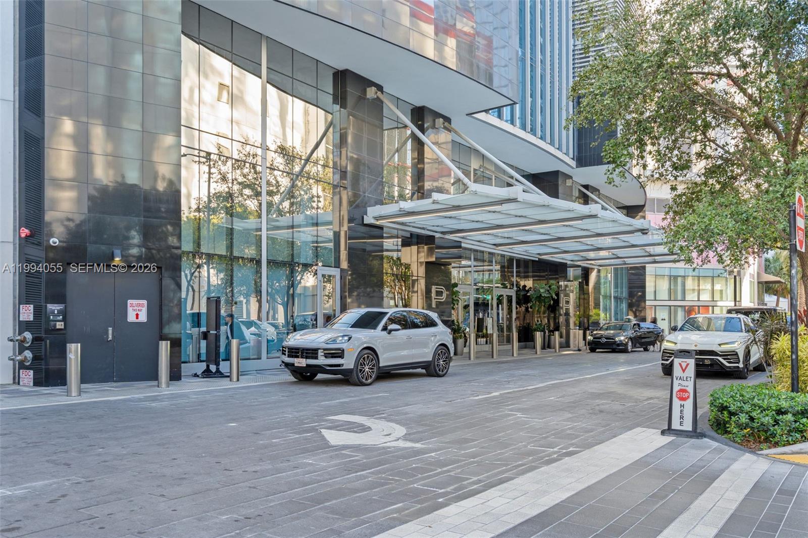 A modern building entrance features a glass canopy, valet parking area, and two luxury SUVs — 851 NE 1st Ave # 1205, Miami FL 33132, MIAMI, FL