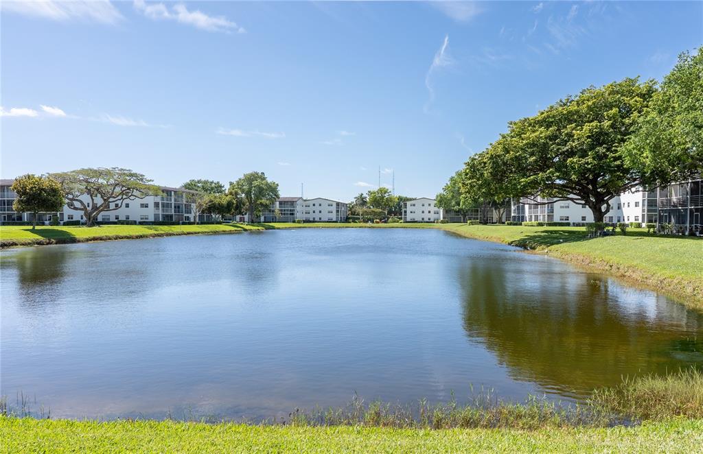 A pond sits in front of several multi-story apartment buildings surrounded by green lawns — 592 FANSHAW O UNIT 592-O, BOCA RATON, FL