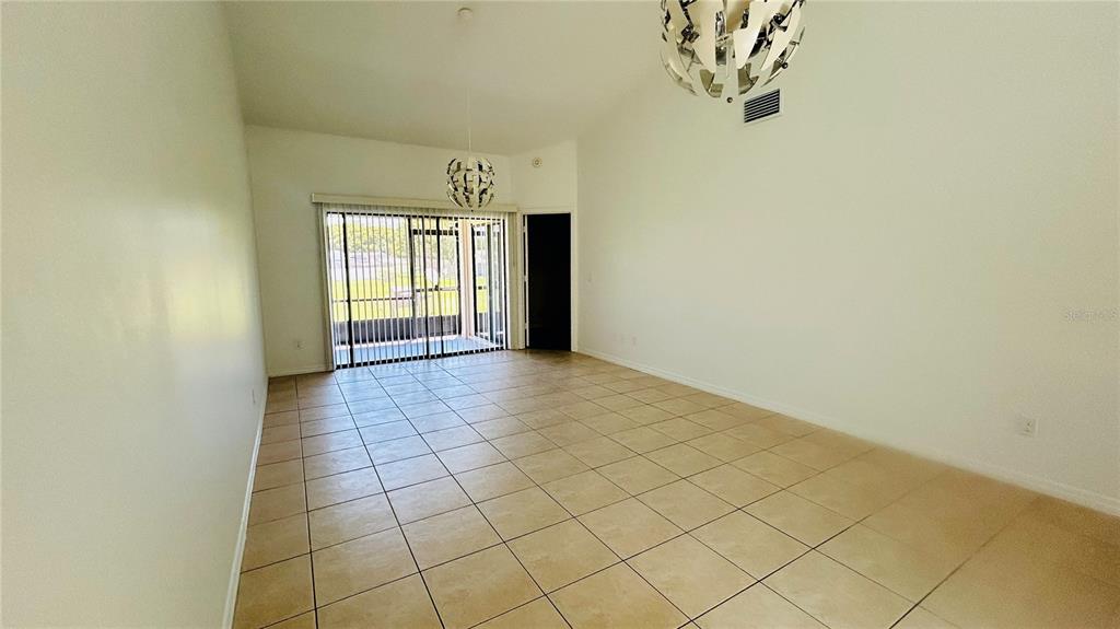 An empty room with light-colored tile flooring, high ceilings, and sliding glass doors — 12121 AUGUSTA WOODS CIRCLE, ORLANDO, FL