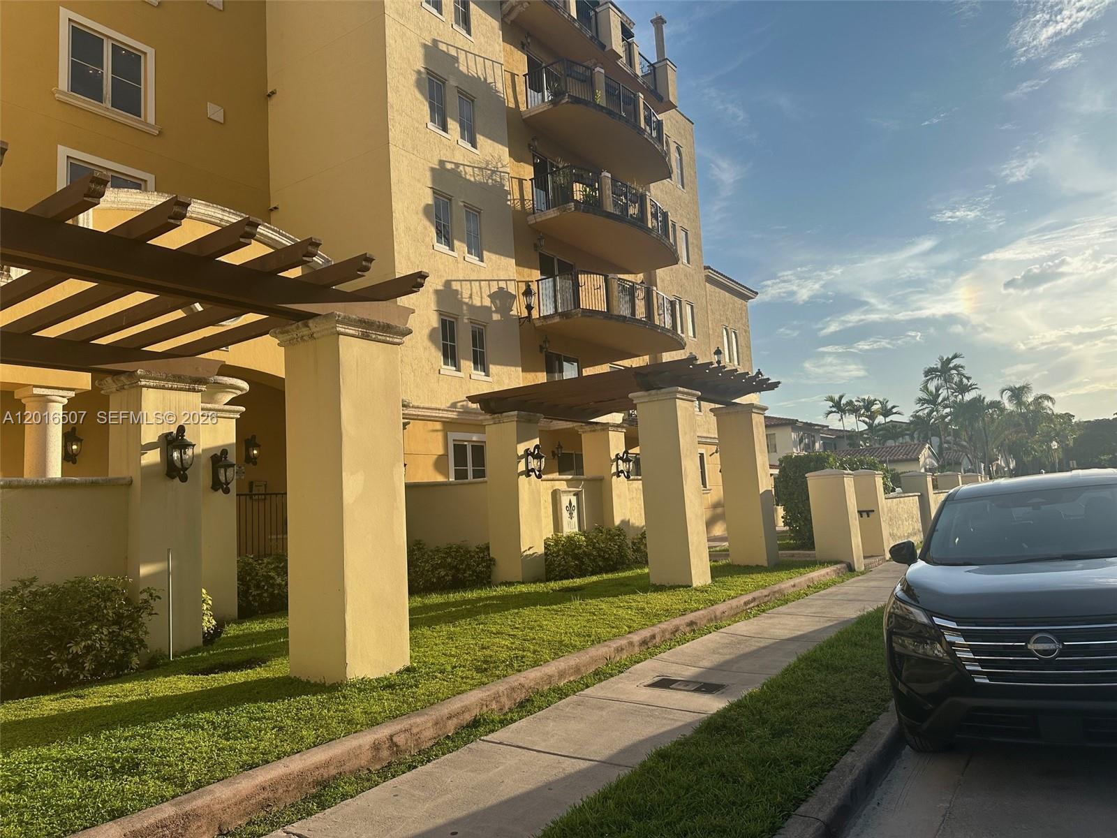 A multi-story yellow apartment building features wooden pergolas over a sidewalk and a parked car — 322 Madeira Ave # 302, Coral Gables FL 33134, CORAL GABLES, FL