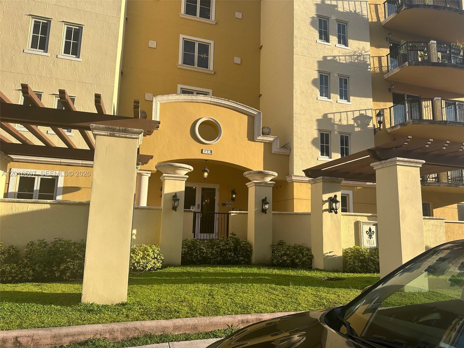 The exterior of a yellow multi-story apartment building features a covered entrance and pergolas — 322 Madeira Ave # 302, Coral Gables FL 33134, CORAL GABLES, FL