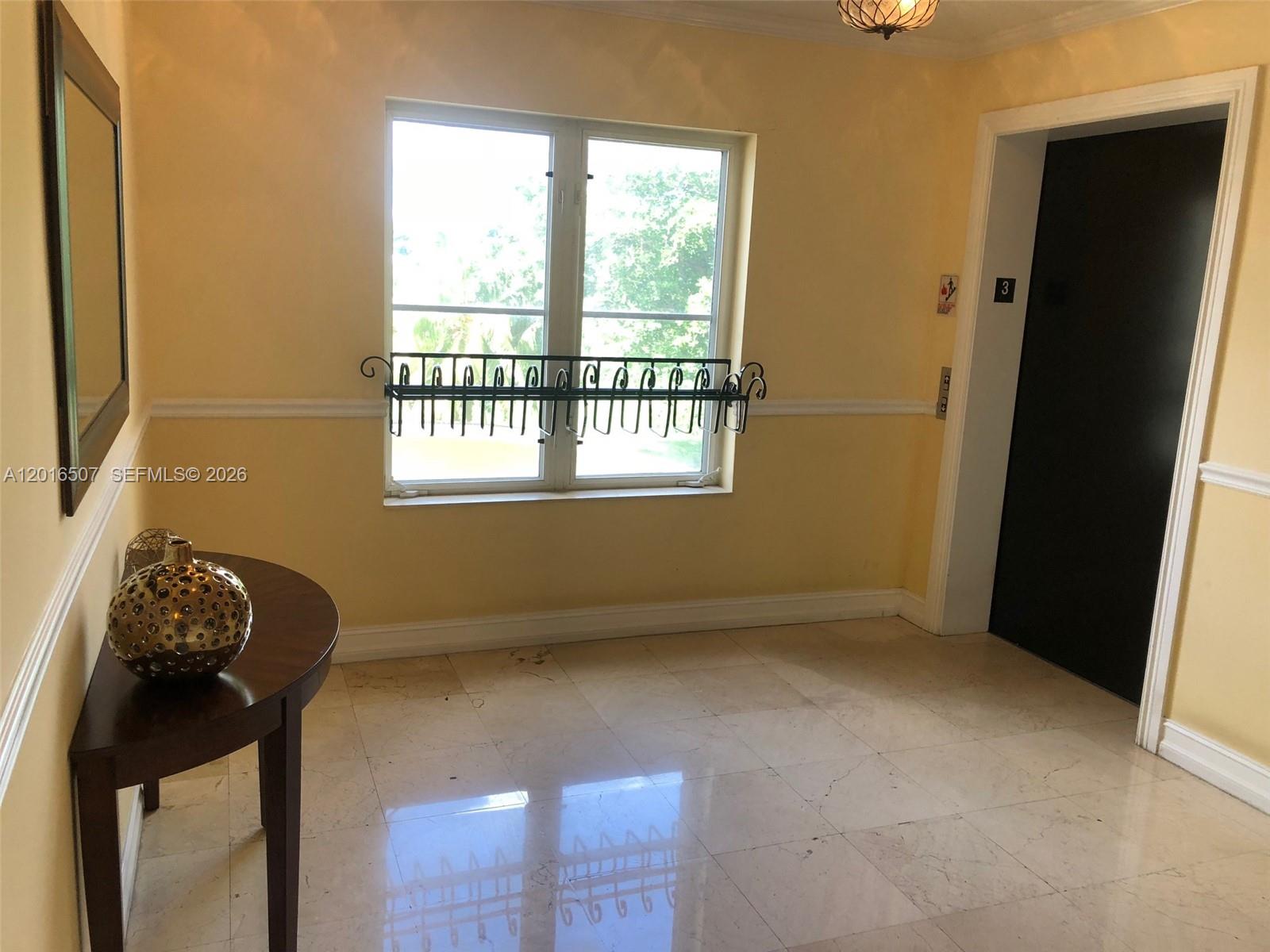 A yellow-walled foyer features a marble floor, a round table, and an elevator door — 322 Madeira Ave # 302, Coral Gables FL 33134, CORAL GABLES, FL