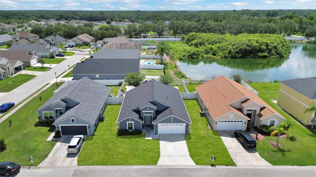 An aerial view shows three suburban houses with driveways and lawns bordering a small lake — 8335 ADELE ROAD, LAKELAND, FL