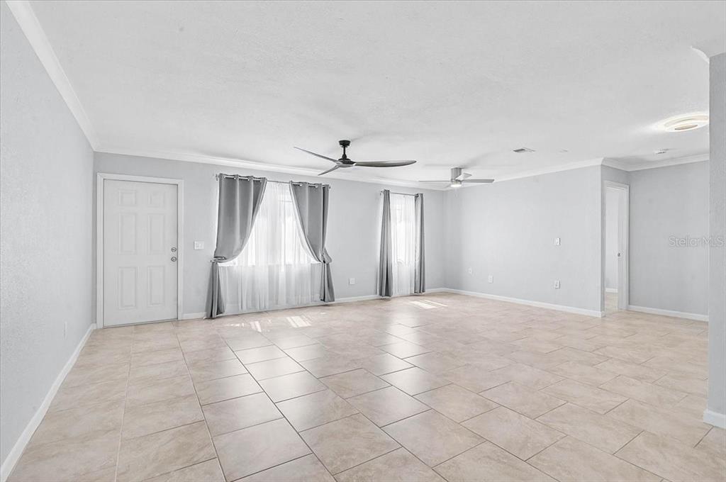 A spacious, empty living room features light tile flooring, white walls, and two ceiling fans — 6652 THORMAN ROAD, PORT CHARLOTTE, FL