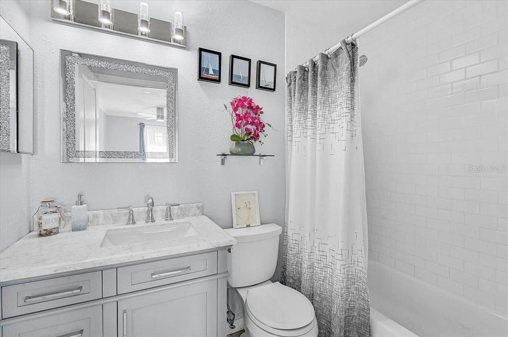A bathroom features a gray vanity, marble countertop, white subway tile shower, and decorative wall art — 6652 THORMAN ROAD, PORT CHARLOTTE, FL