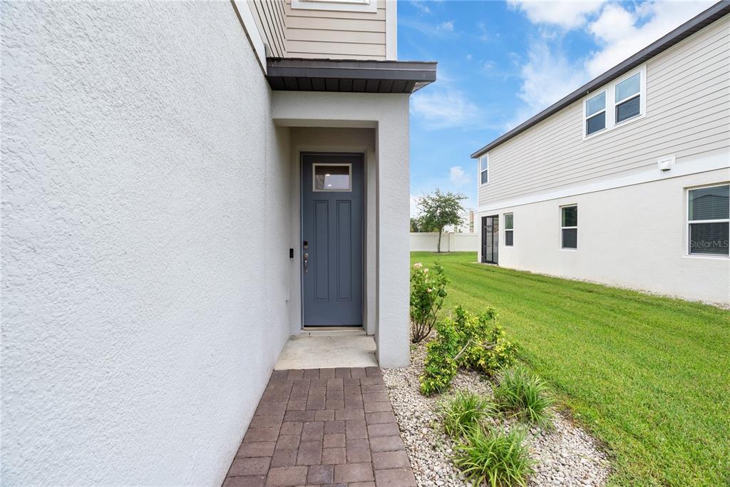 A gray front door is recessed into a white stucco wall beside a paved walkway — 15187 WILLOW ARBOR CIRCLE, ORLANDO, FL