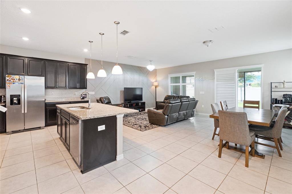 An open-concept kitchen and living area features dark cabinetry, a granite island, and tile flooring — 15187 WILLOW ARBOR CIRCLE, ORLANDO, FL