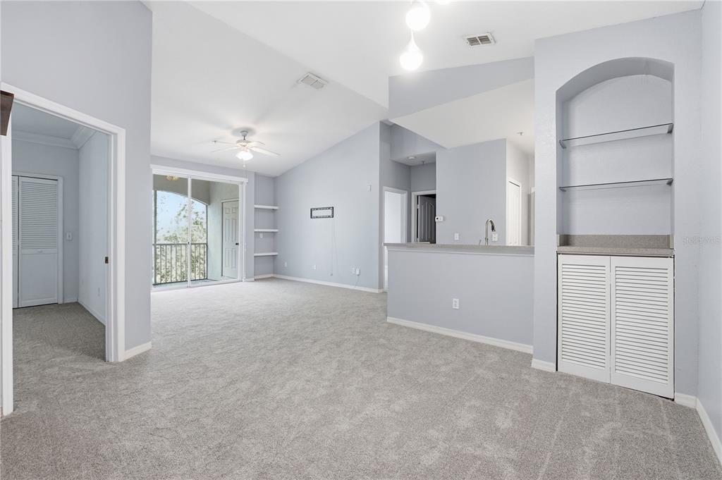 An open-concept living area features gray carpeting, vaulted ceilings, a balcony, and built-in shelving — 2525 MAITLAND CROSSING WAY UNIT 304, ORLANDO, FL