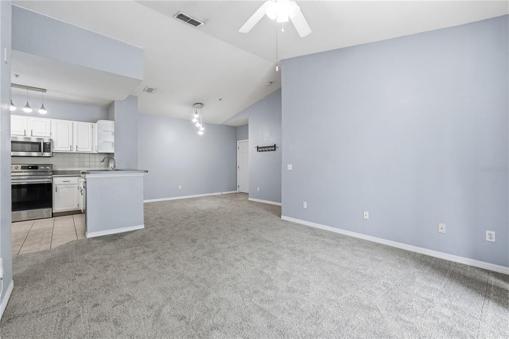 A living room with gray carpet and light blue walls opens to a kitchen area — 2525 MAITLAND CROSSING WAY UNIT 304, ORLANDO, FL