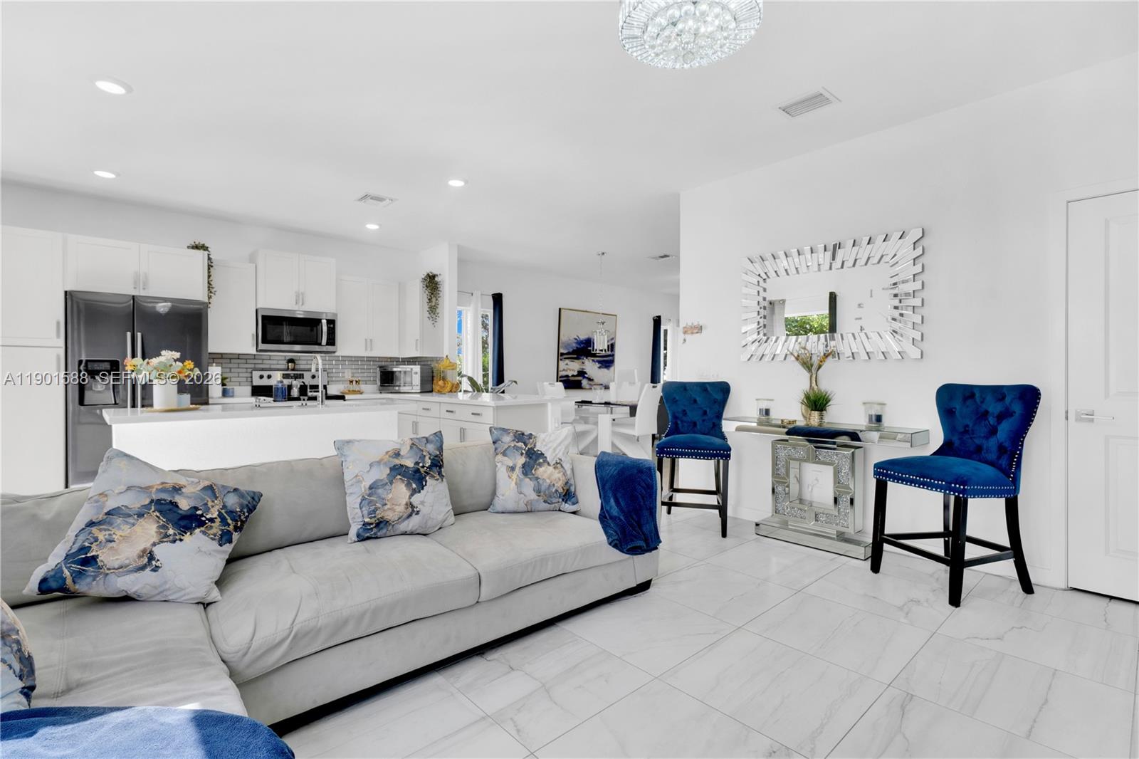 A modern open-concept living room and kitchen featuring white cabinetry, tile flooring, and blue accents — 856 SE 16th Ct, Homestead FL 33034, HOMESTEAD, FL