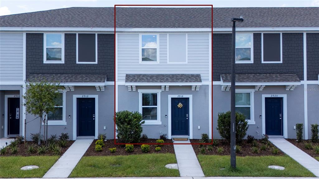 A row of modern townhomes with gray siding, dark blue doors, and small front lawns — 2916 SKYLINE LOOP, KISSIMMEE, FL