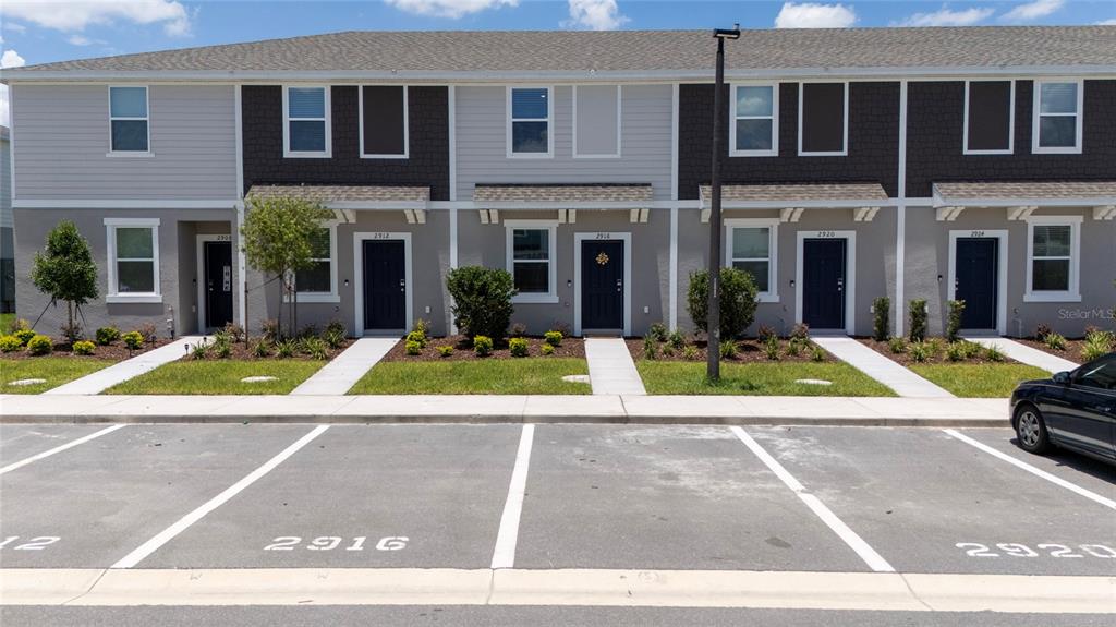 A row of two-story townhomes with dark doors and assigned parking spaces in front — 2916 SKYLINE LOOP, KISSIMMEE, FL